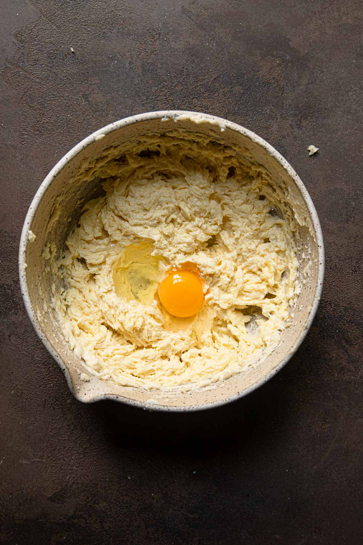 A mixing bowl with creamed butter and sugar and an egg.