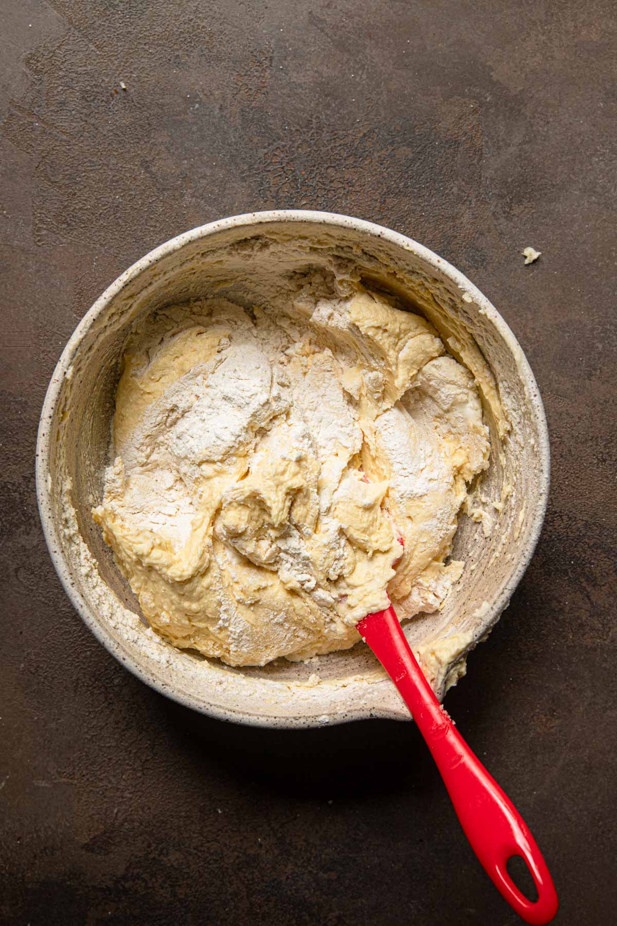 A mixing bowl with a cake batter and some flour and a spatula.