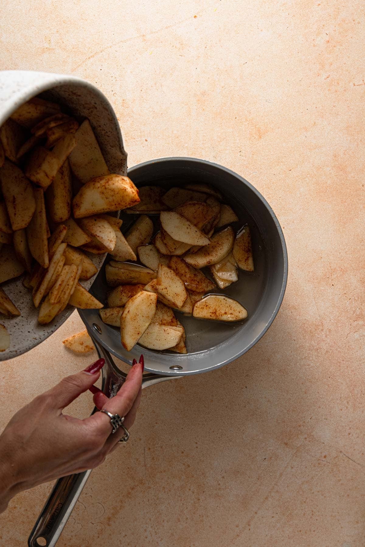 A hand adding apples to sugar syrup in a pan.