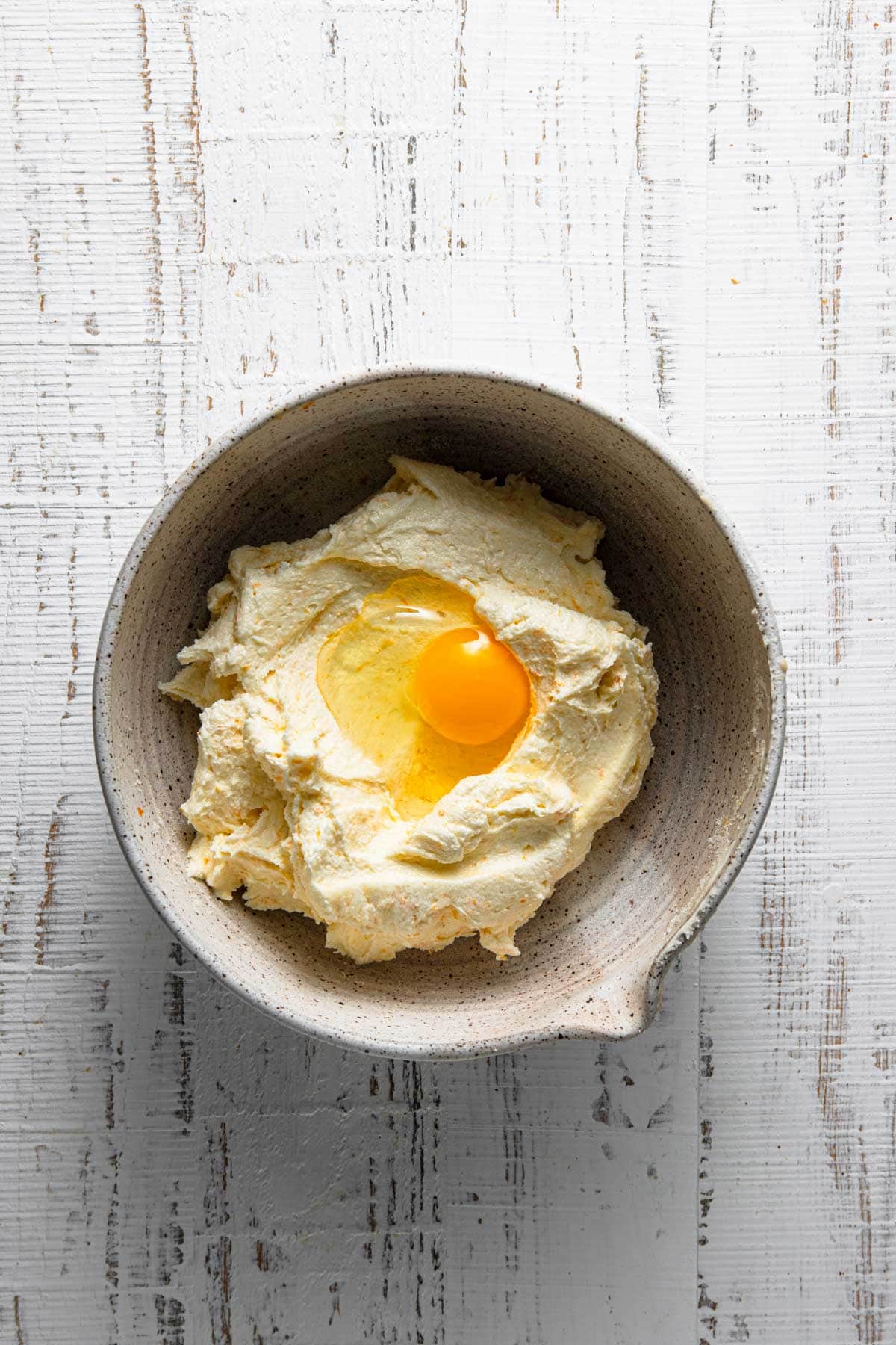 A bowl with creamed butter and sugar and an egg.