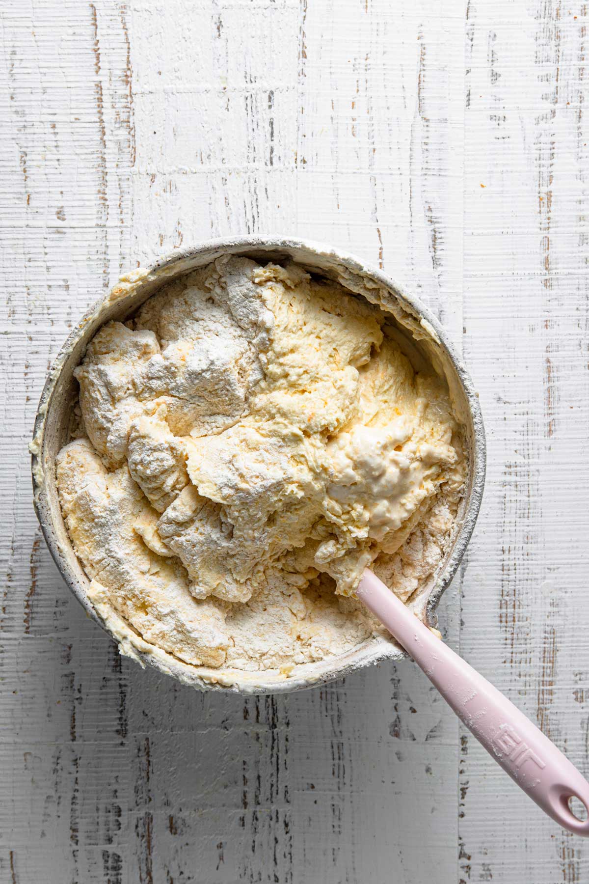 A bowl with a spatula incorporating flour into an orange cake batter.