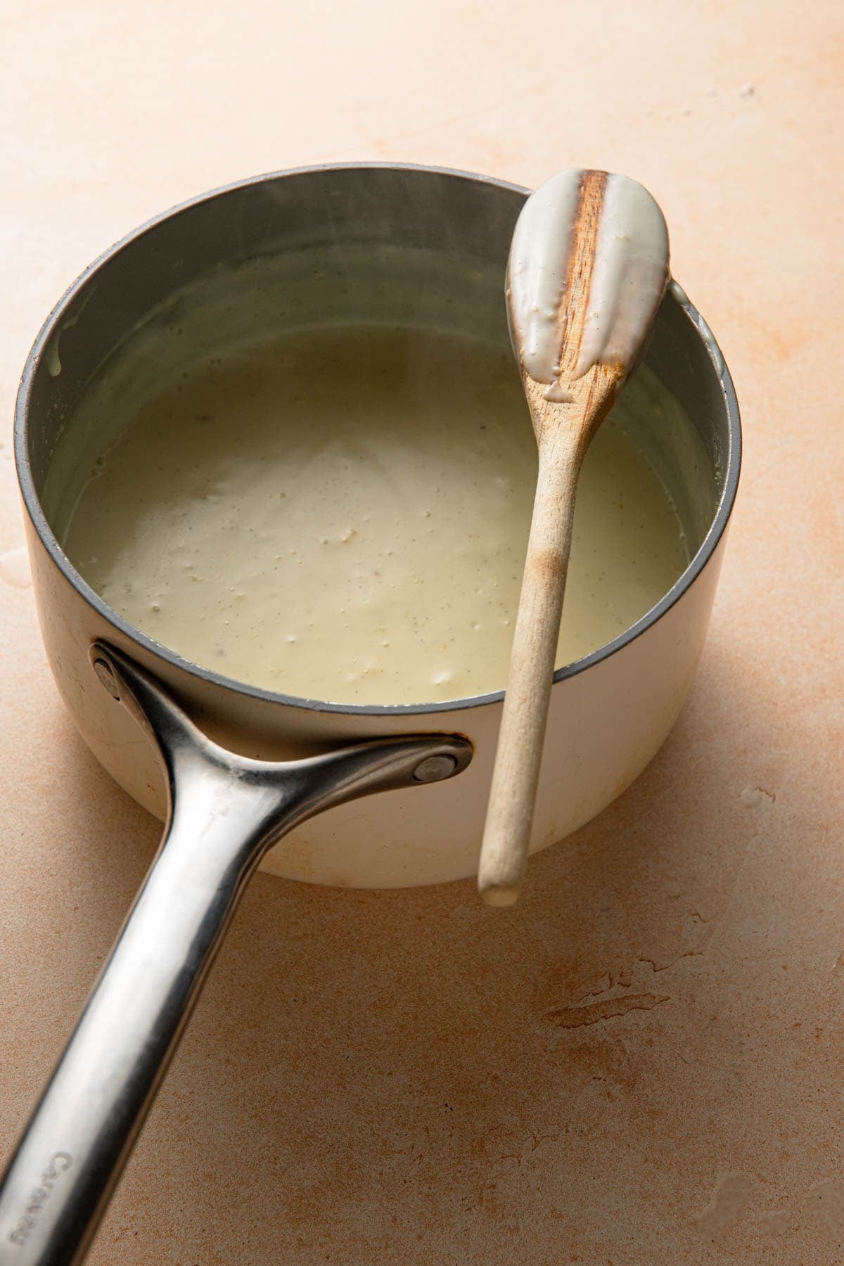 A saucepan with custard cream and a wooden spoon.