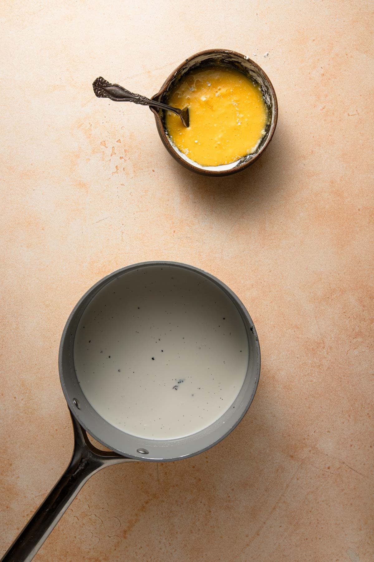 A saucepan with cream and milk and a bowl with egg yolks mixed with cornstarch.