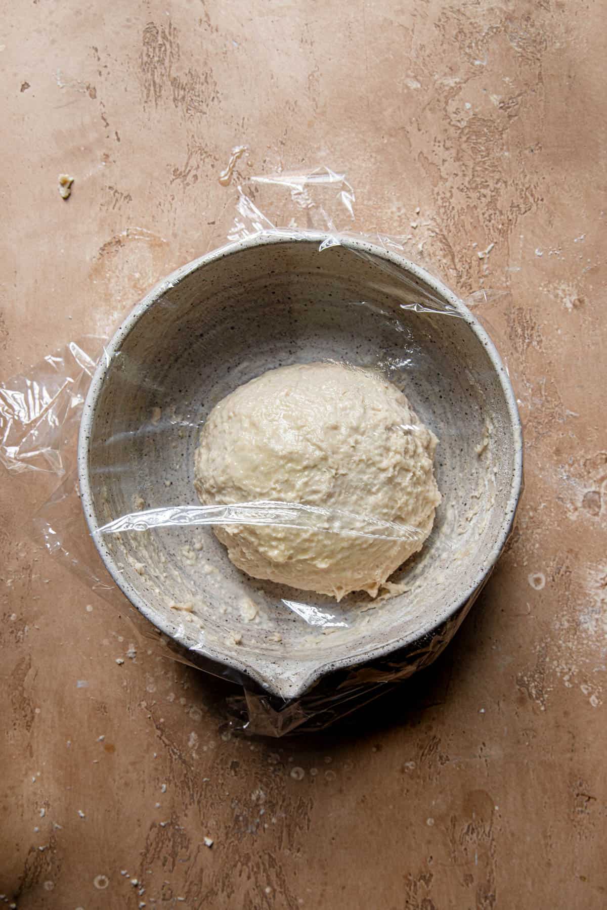raw dough in a bowl topped with plastic wrap.