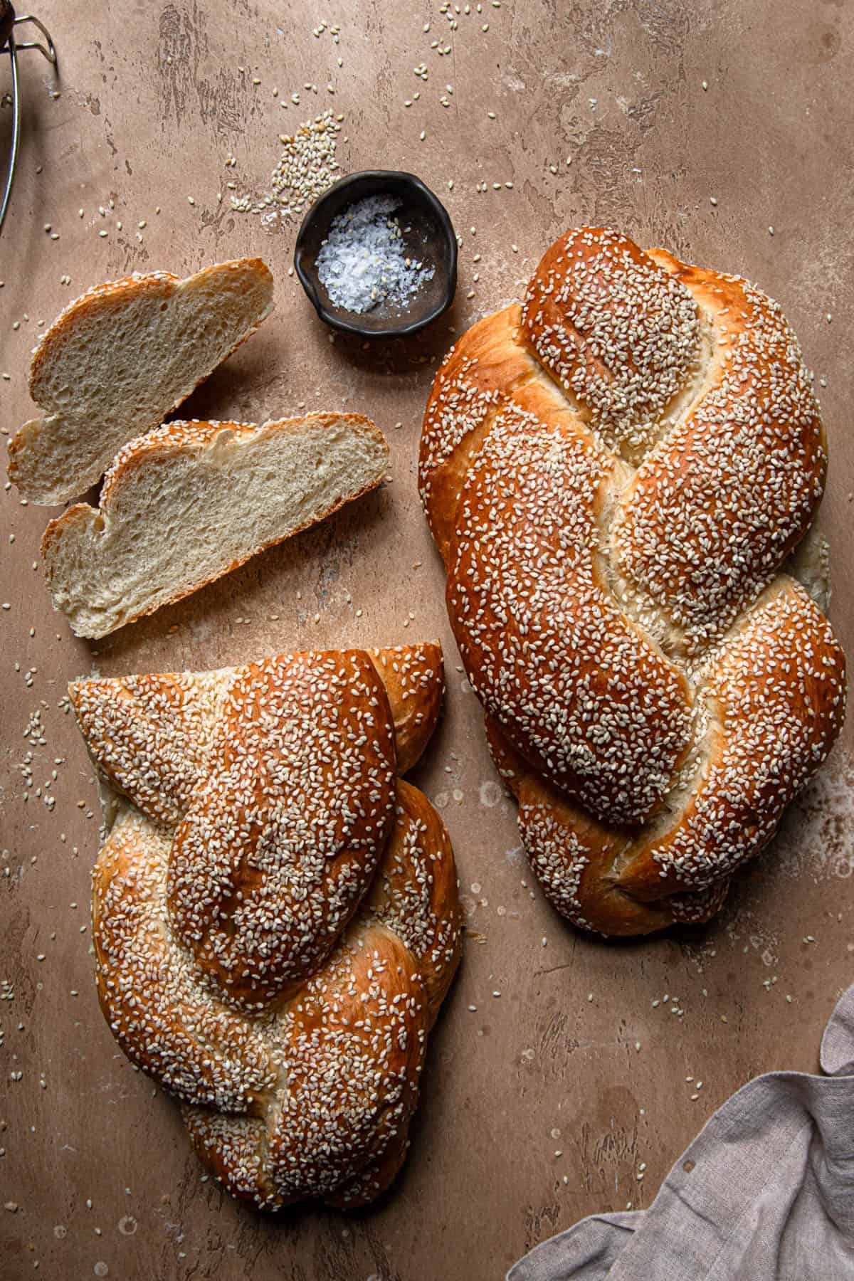 Two vegan challah topped with sesame seeds, one sliced loaf.