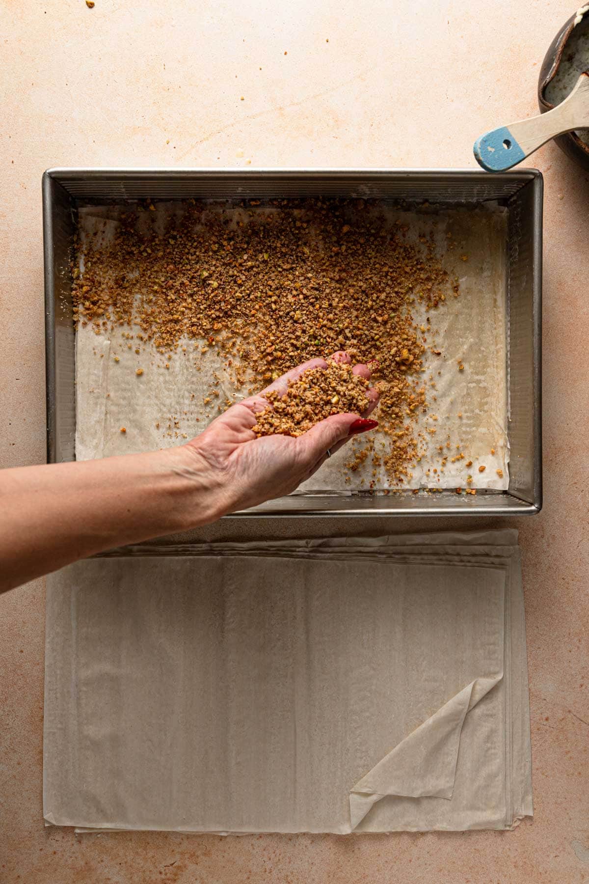 Hand sprinkling nuts over phyllo sheet.