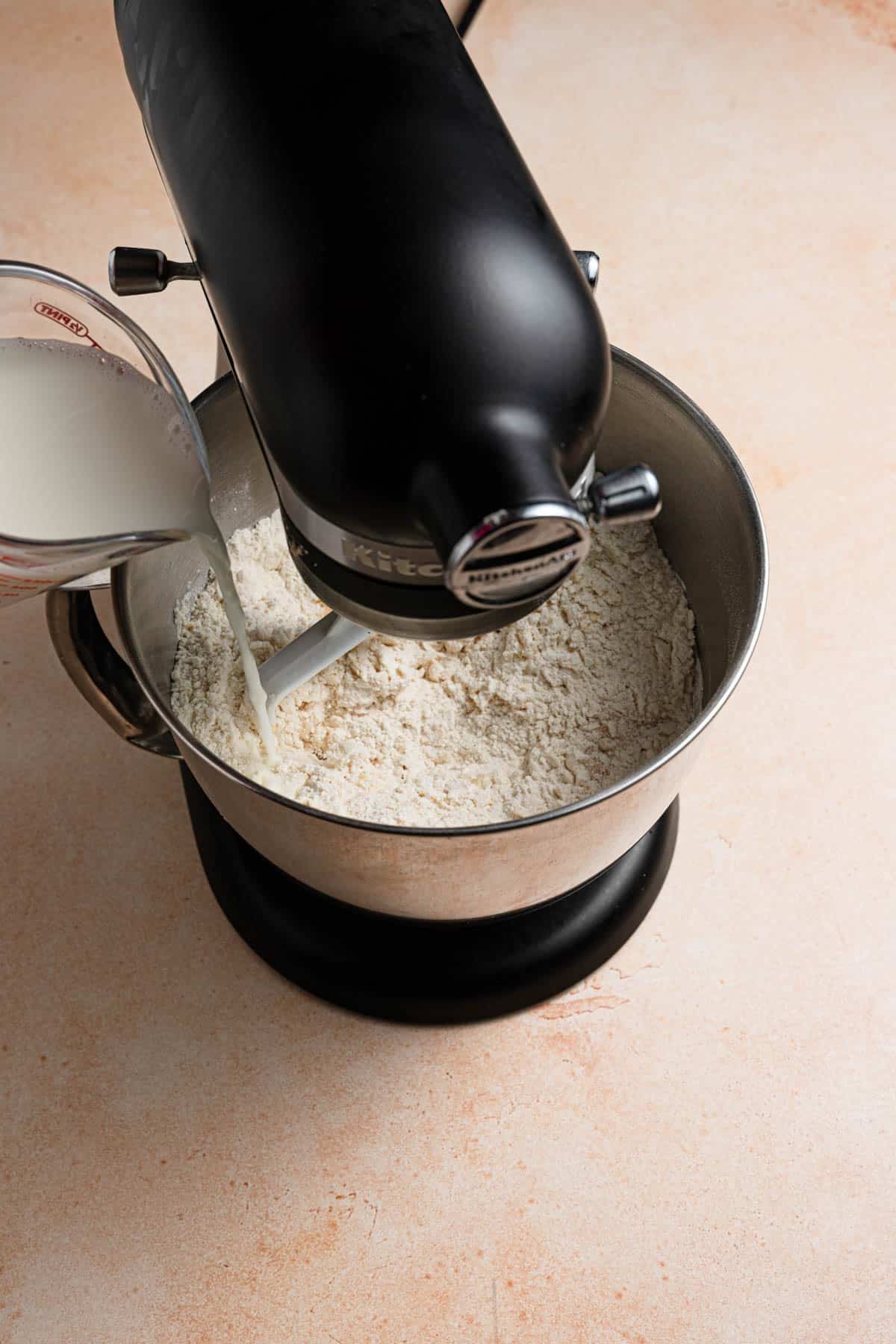 Pouring milk into dry ingredients in a mixer bowl.