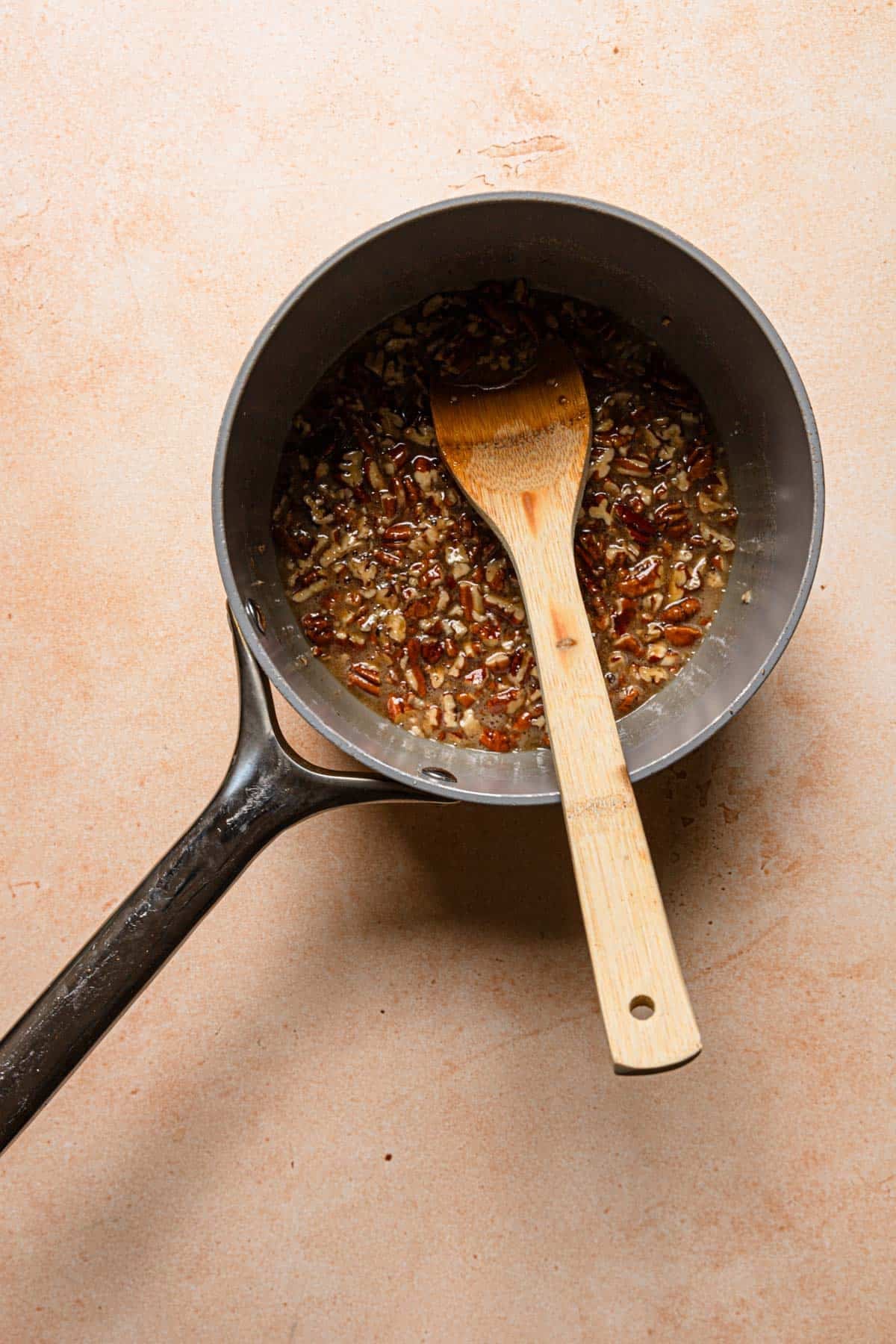 a saucepan with honey syrup and chopped pecans and a wooden spoon.