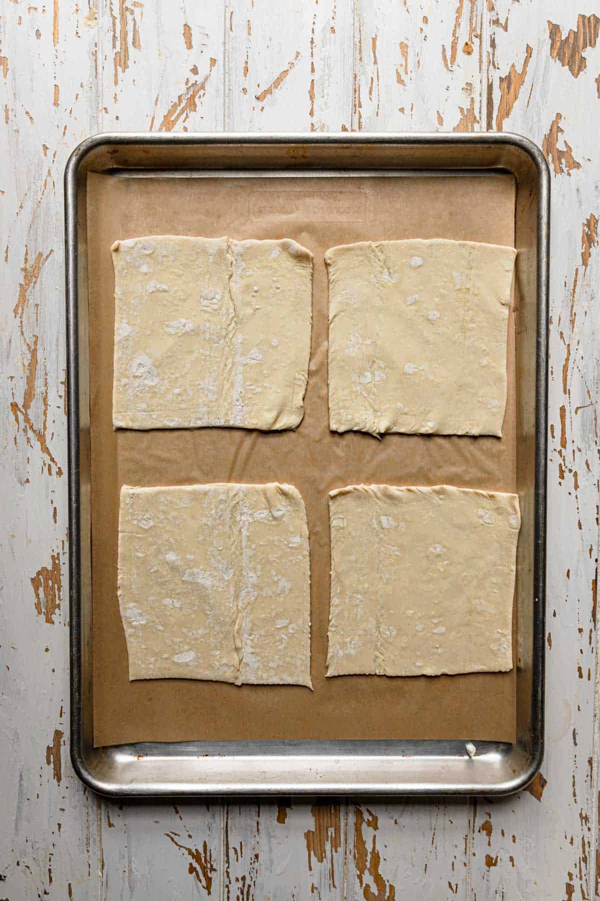 a baking sheet topped with parchment paper and puff pastry squares.
