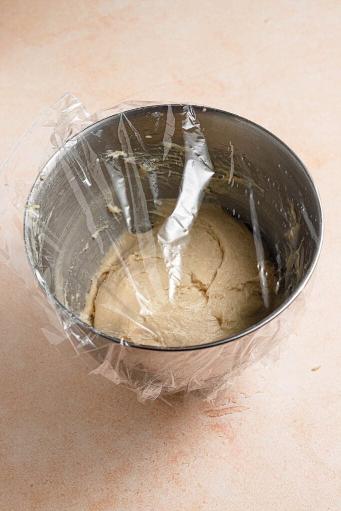 Dough inside a bowl covered with plastic wrap.