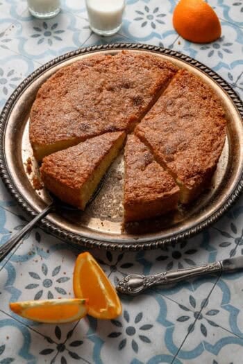 Orange cake with cups of milk and slices of orange.