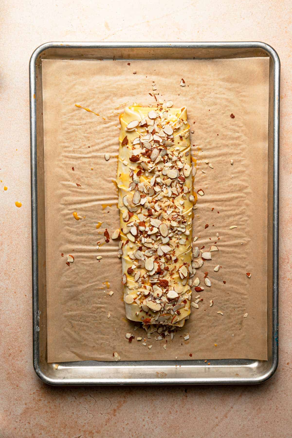 A braided pastry on top of a a baking pan, topped with sliced almonds.