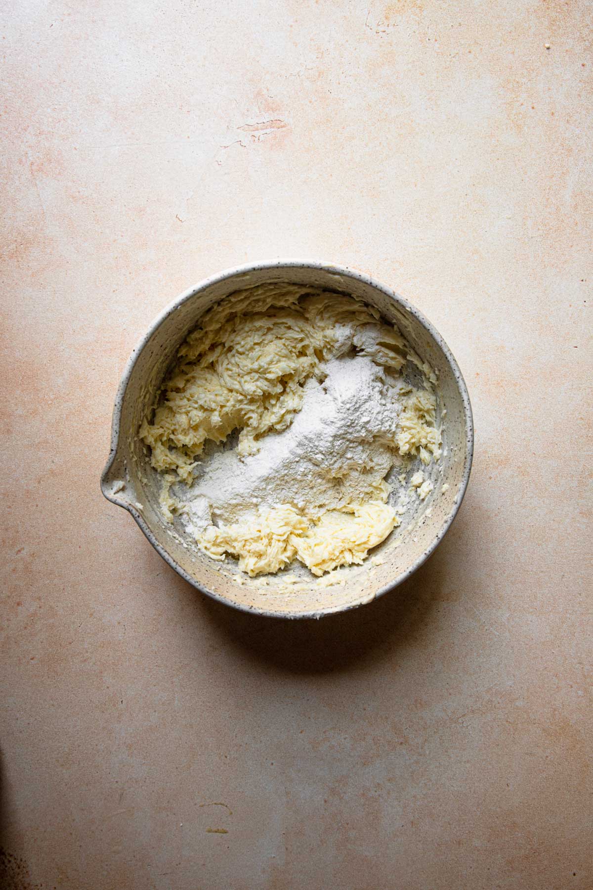 A bowl with creamed butter mixture and dry flour.