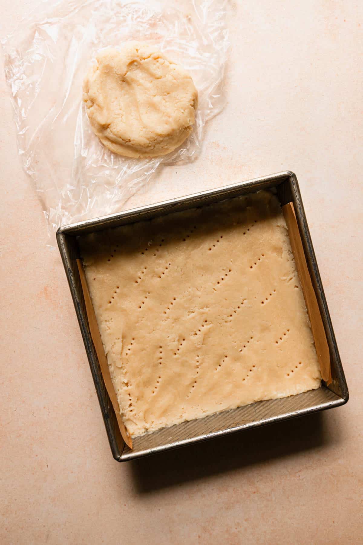 A pan with raw shortbread dough, next to a piece of dough on topped on plastic wrap.