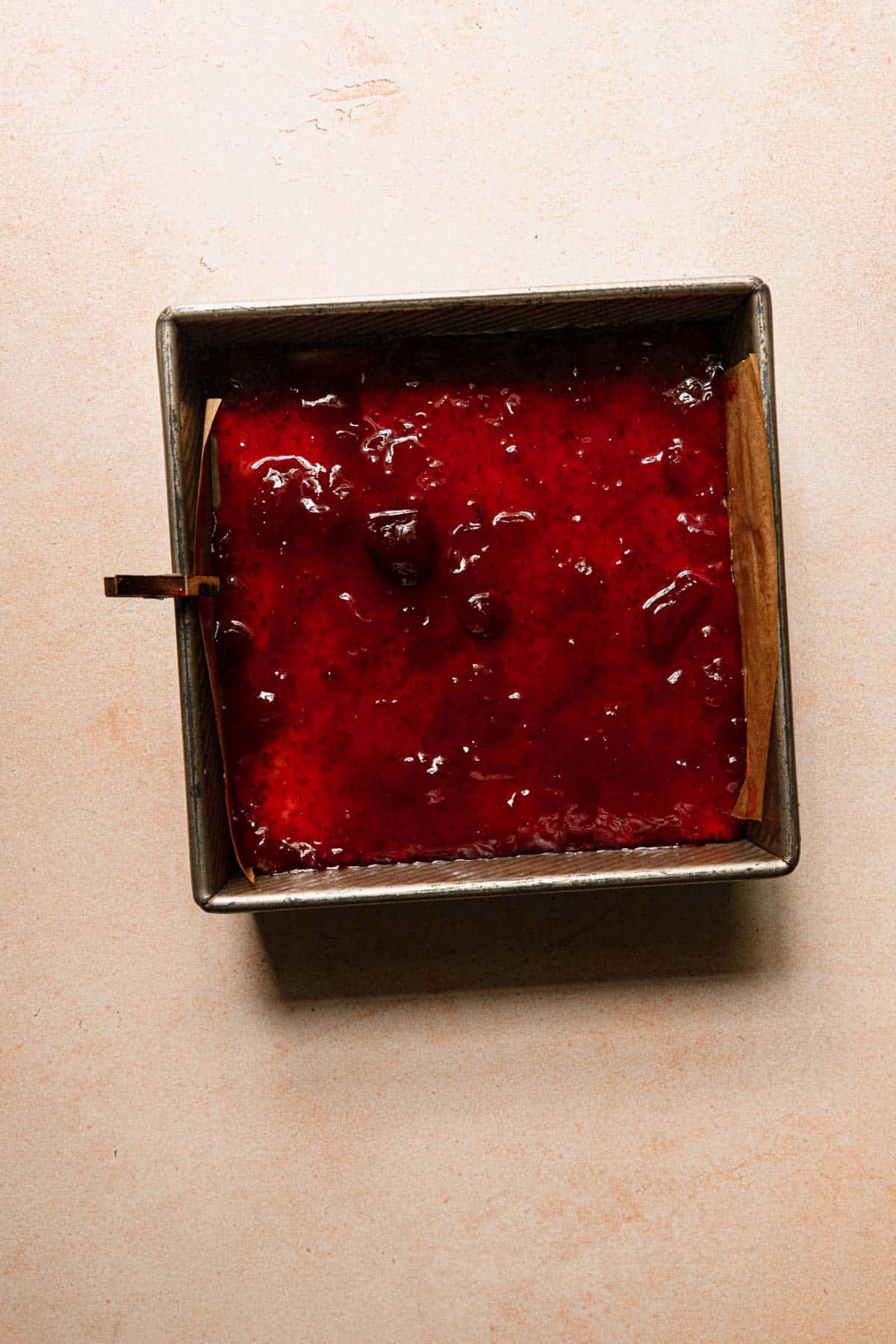 A pan with shortbread dough topped with strawberry preserves.