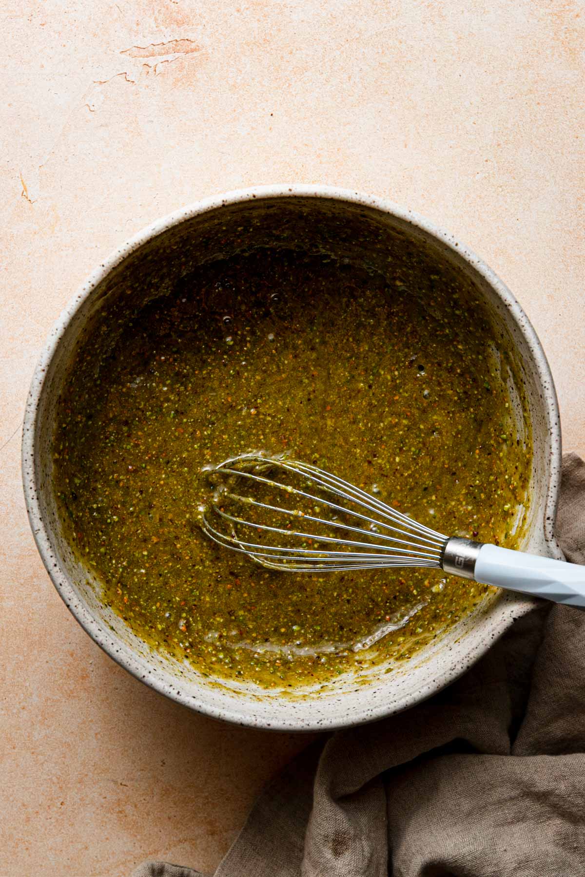 A large bowl pistachio mixture in it. A whisk in the bowl and a napkin next to it.