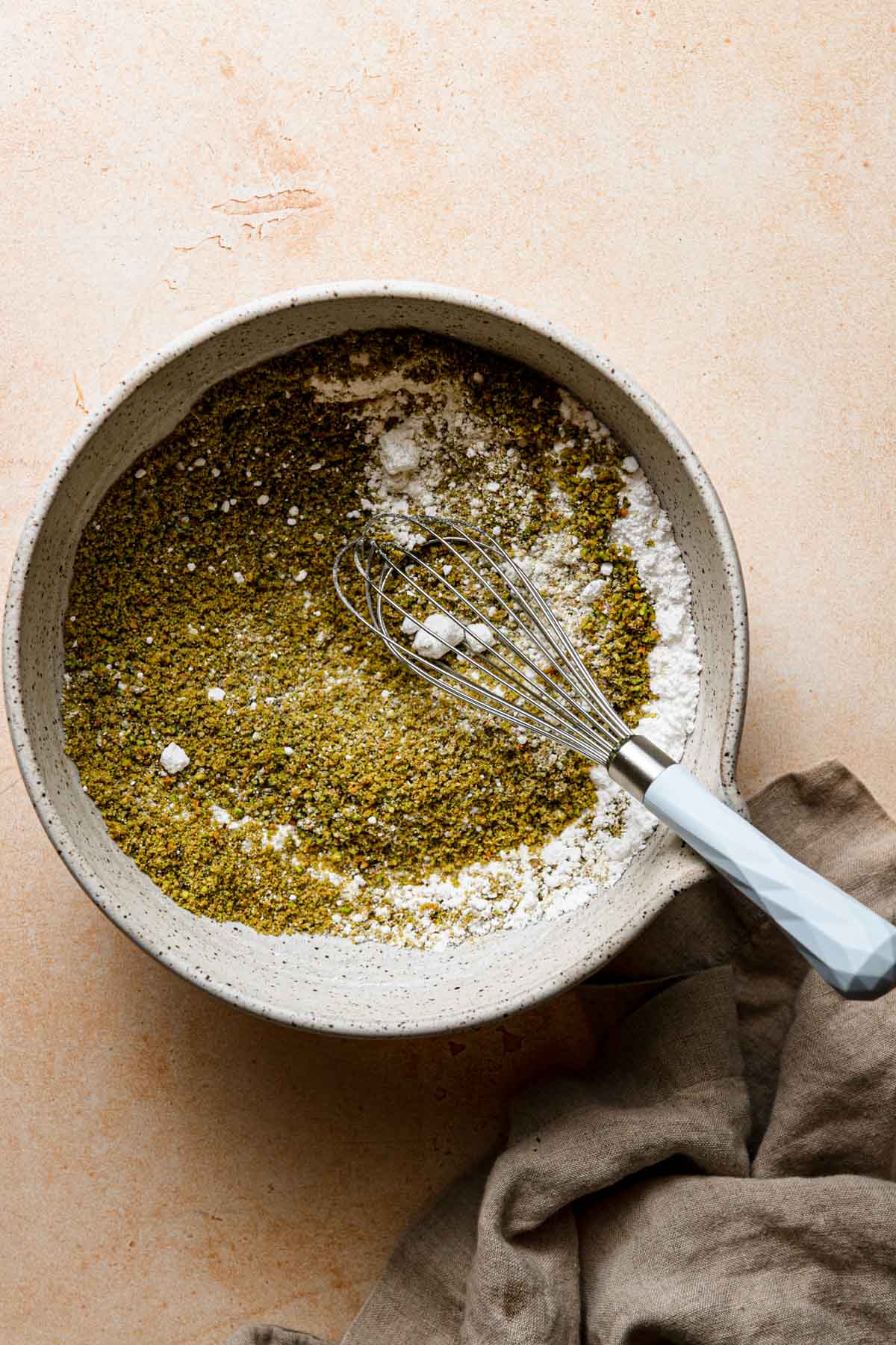 A large bowl with ground nuts, and powered sugar. A whisk in the bowl and a napkin next to it.