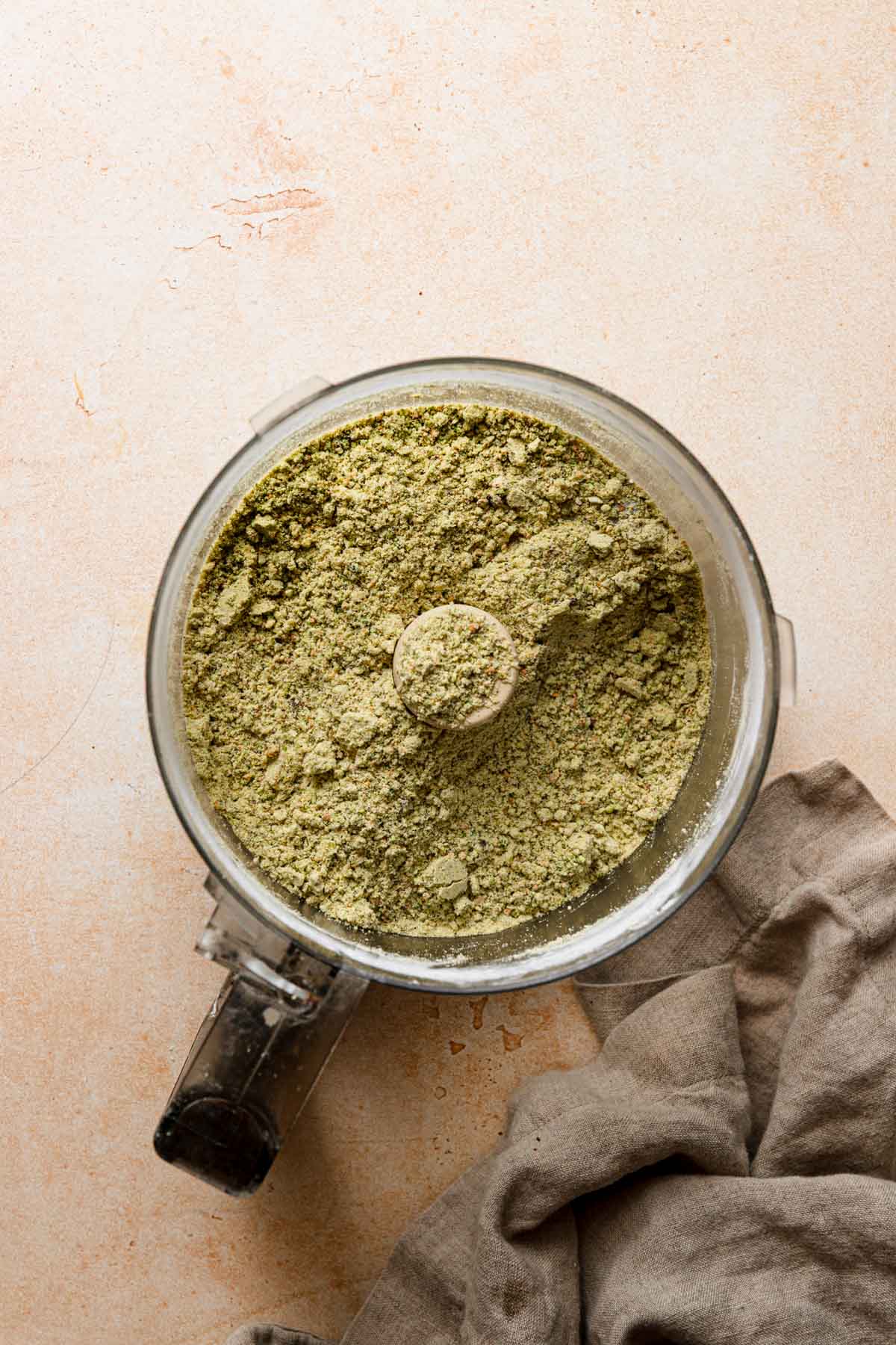 A bowl of a food processor processed pistachios. A napkin next to it.