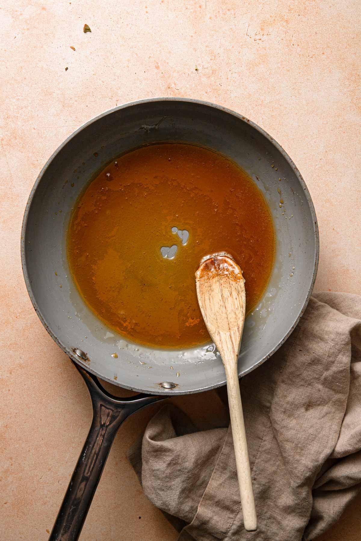 A wide skillet with caramelized sugar and a wooden spoon.