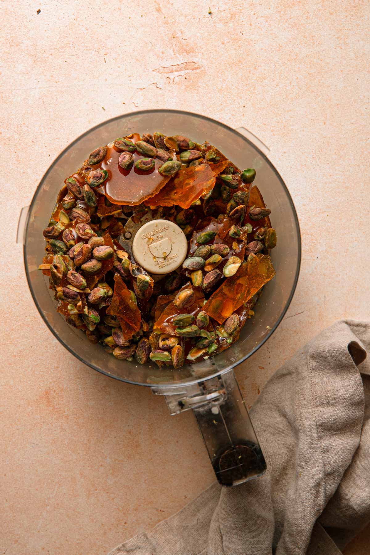 A food processor bowl with pistachio praline chunks.