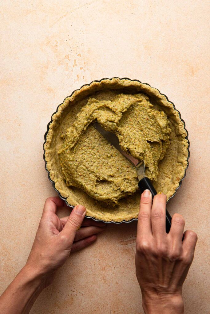 A hand spreading pistachio cream into a tart shell.