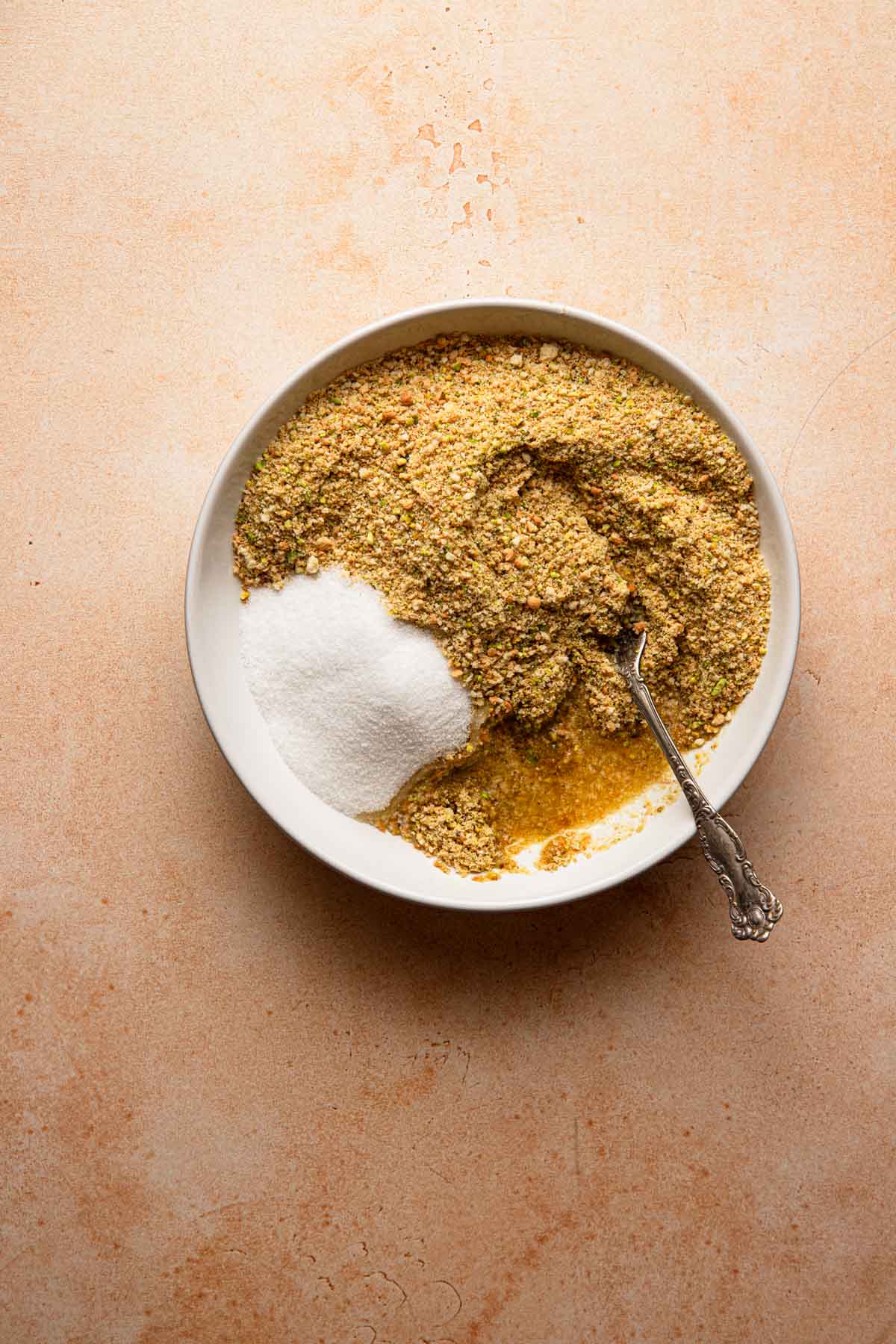 A bowl with cookie crumbs, ground pistachios and sugar with a fork.