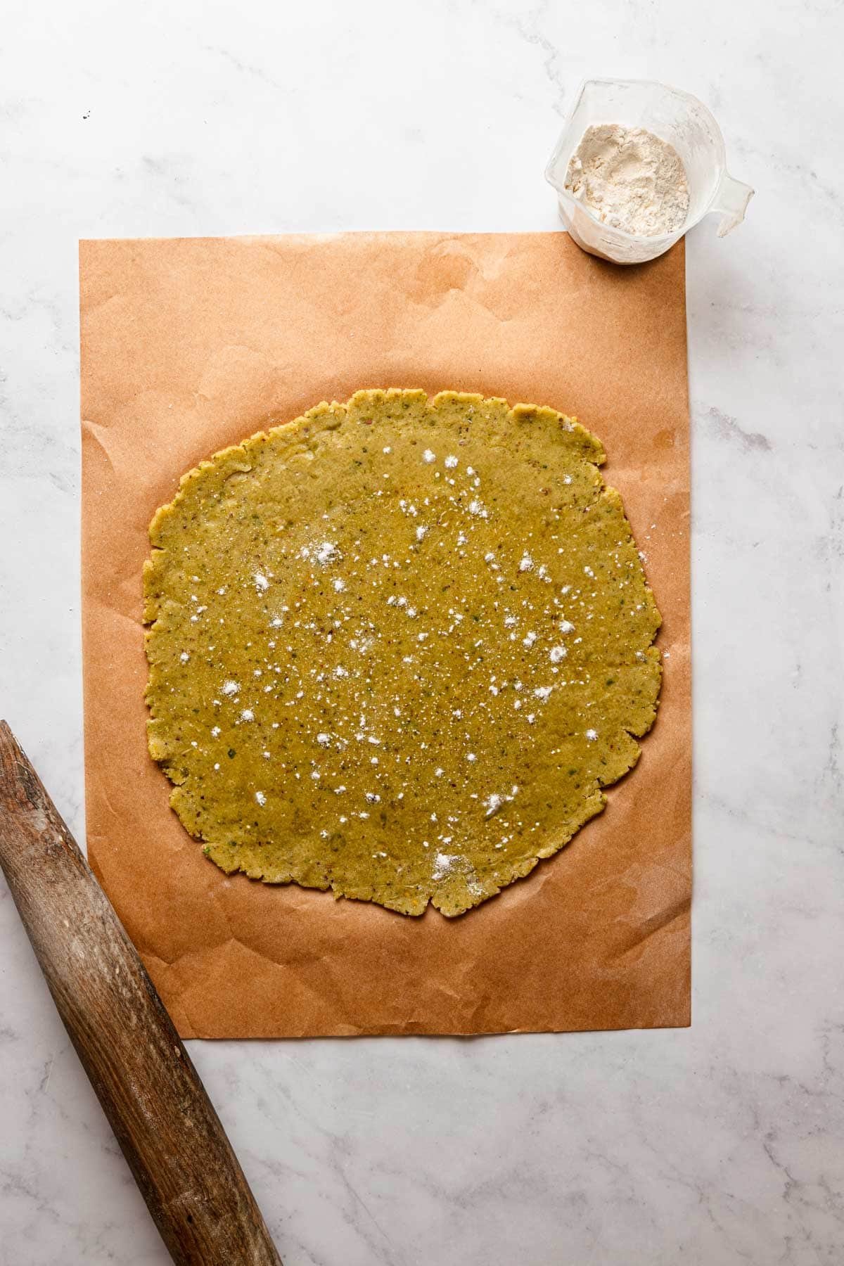 Dough over a piece of parchment paper with a rolling pin next to it.