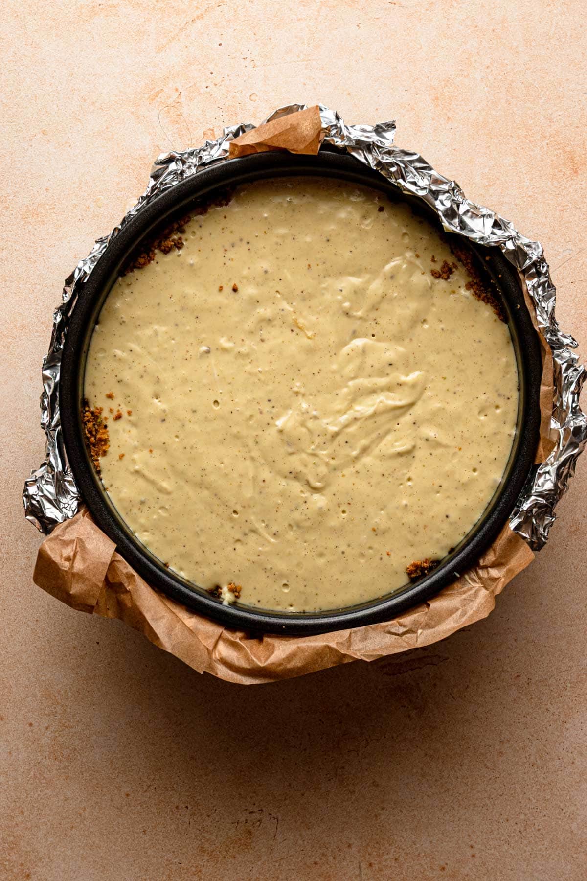A pan wrapped with aluminum foil and filled with pistachio batter.