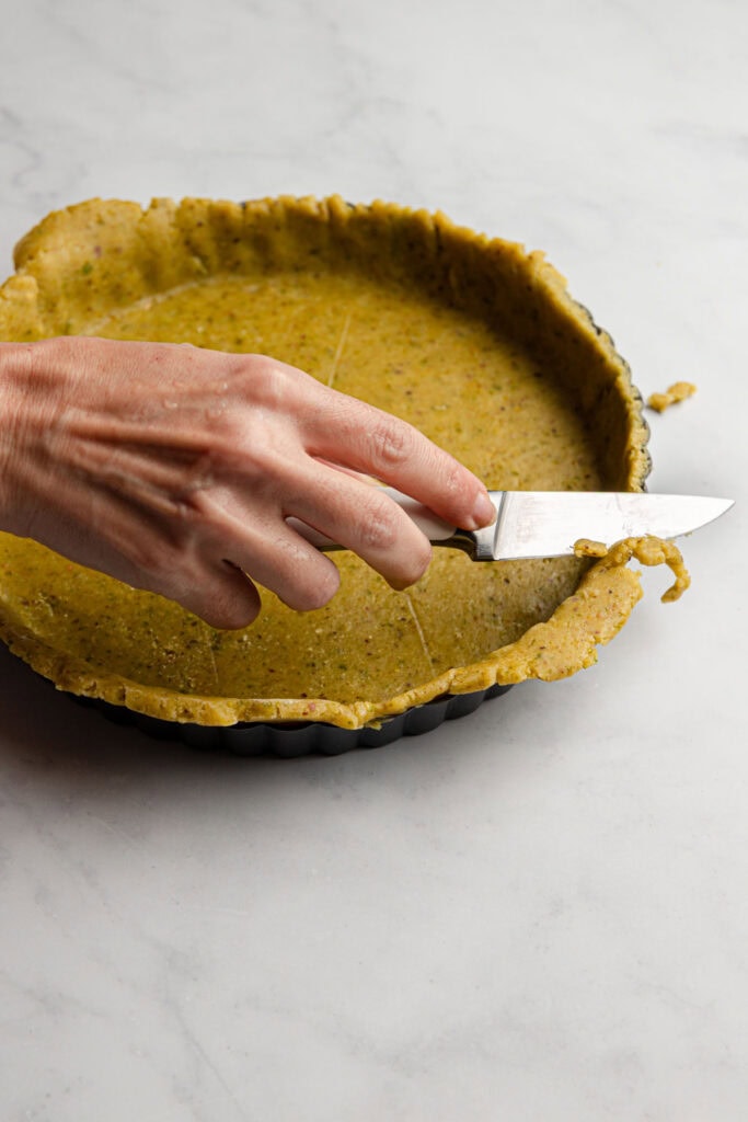 a hand cutting access dough with a knife.