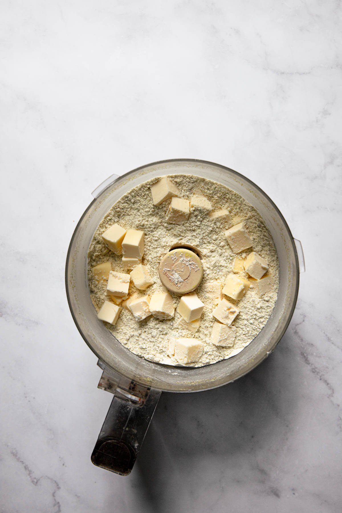 A food processor bowl with flour and butter pieces.