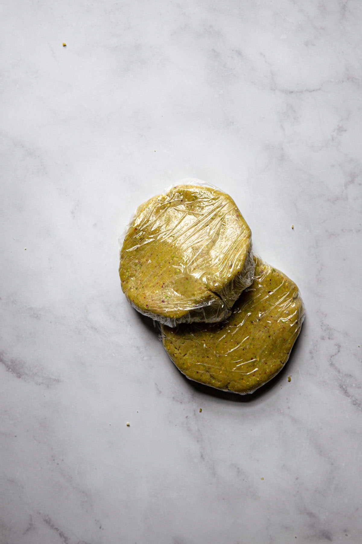 Pistachio dough disks wrapped in plastic wrap.