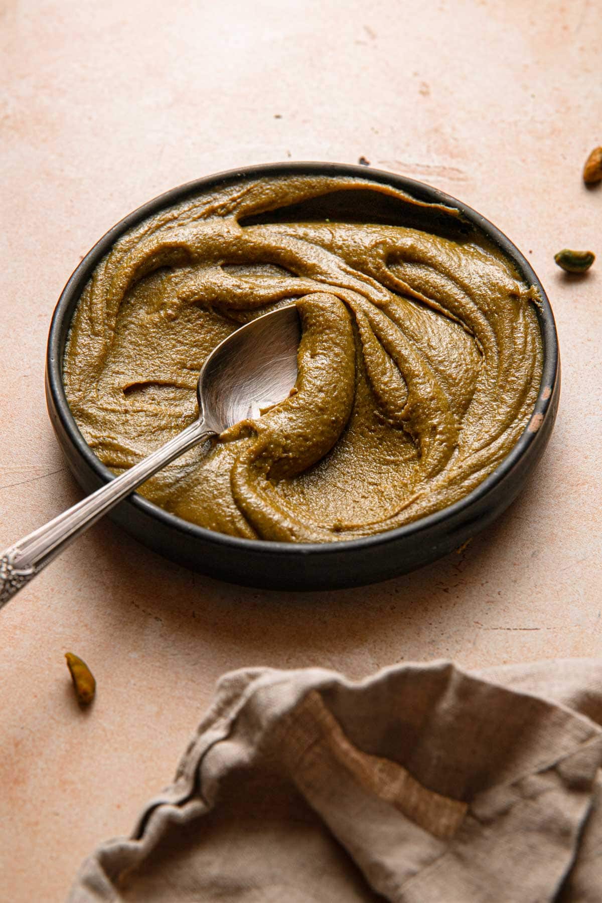 Pistachio caramel paste in a bowl with a spoon and a napkin.