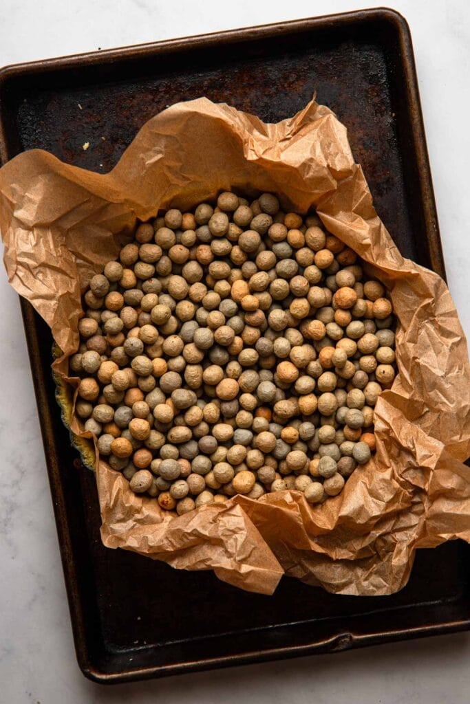 A tart shell with pie weights on top of a pan.