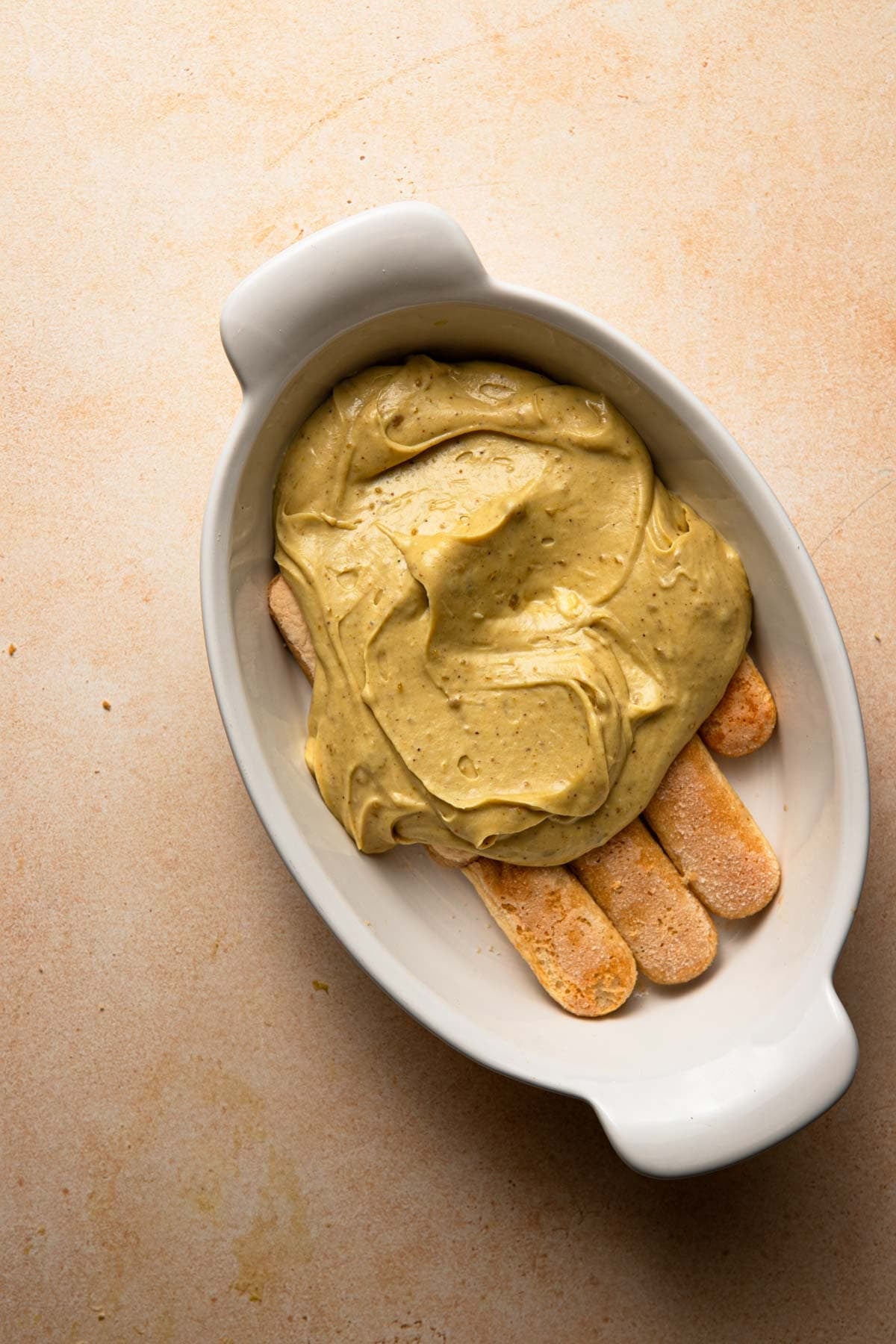 An oval dish with a layer of ladyfingers and cream on top.