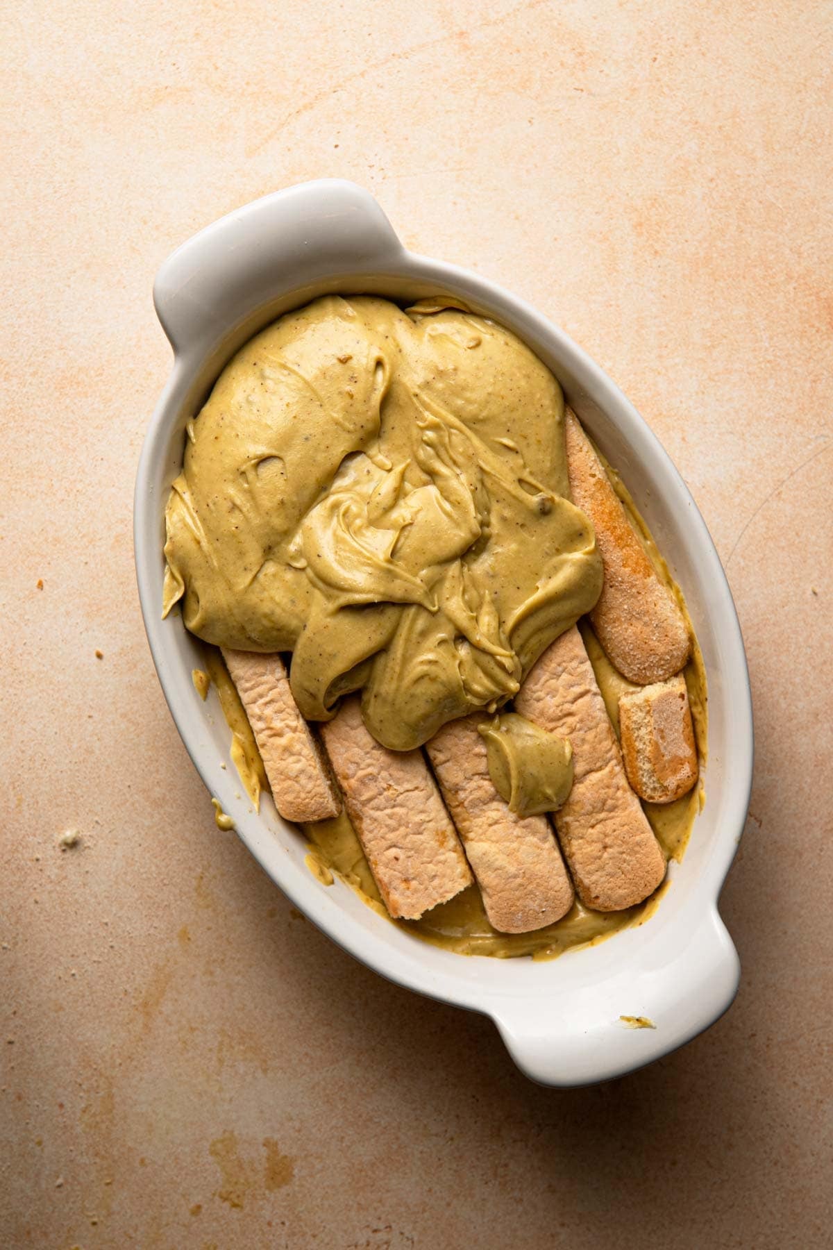An oval dish with a layer of ladyfingers and cream on top.
