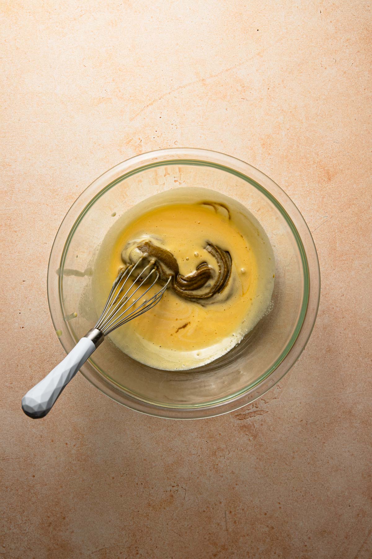 a bowl with egg mixture, pistachio paste and a whisk.