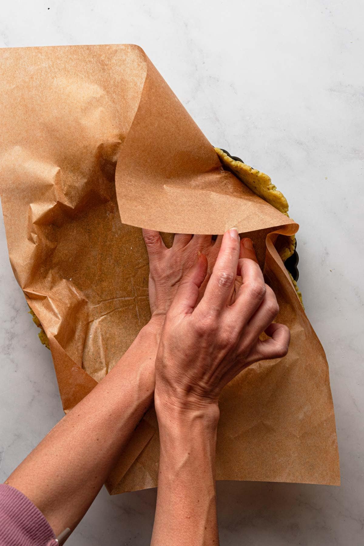 hands pressing dough into a pan using parchment paper.