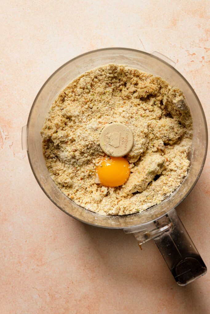 a food processor bowl with flour mixture and an egg yolk.