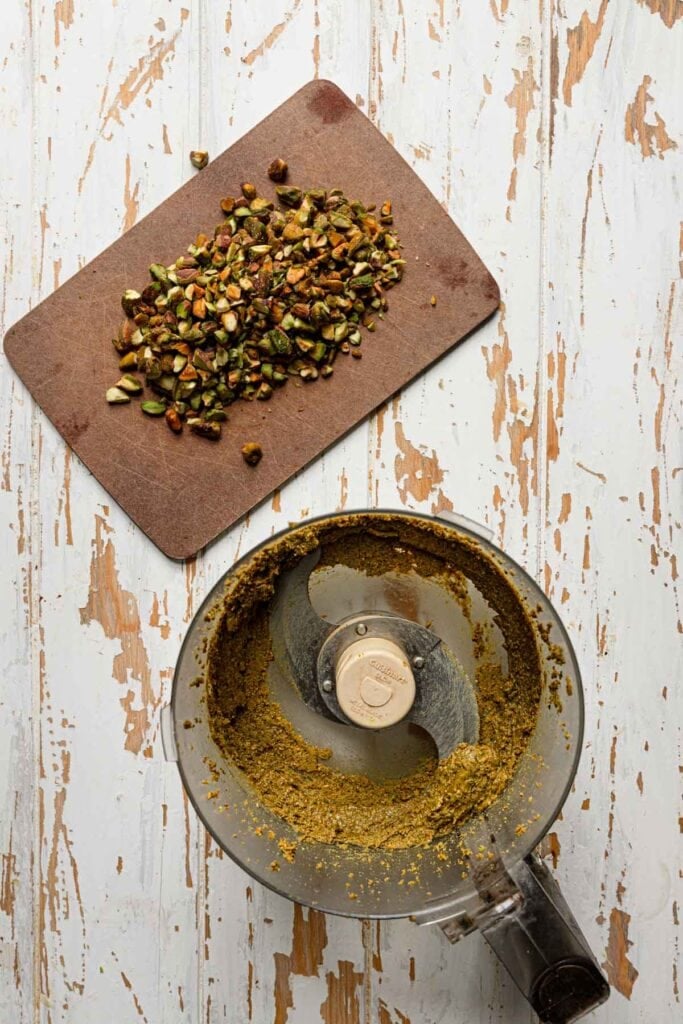 A food processor with pistachio paste next to chopped pistachios.