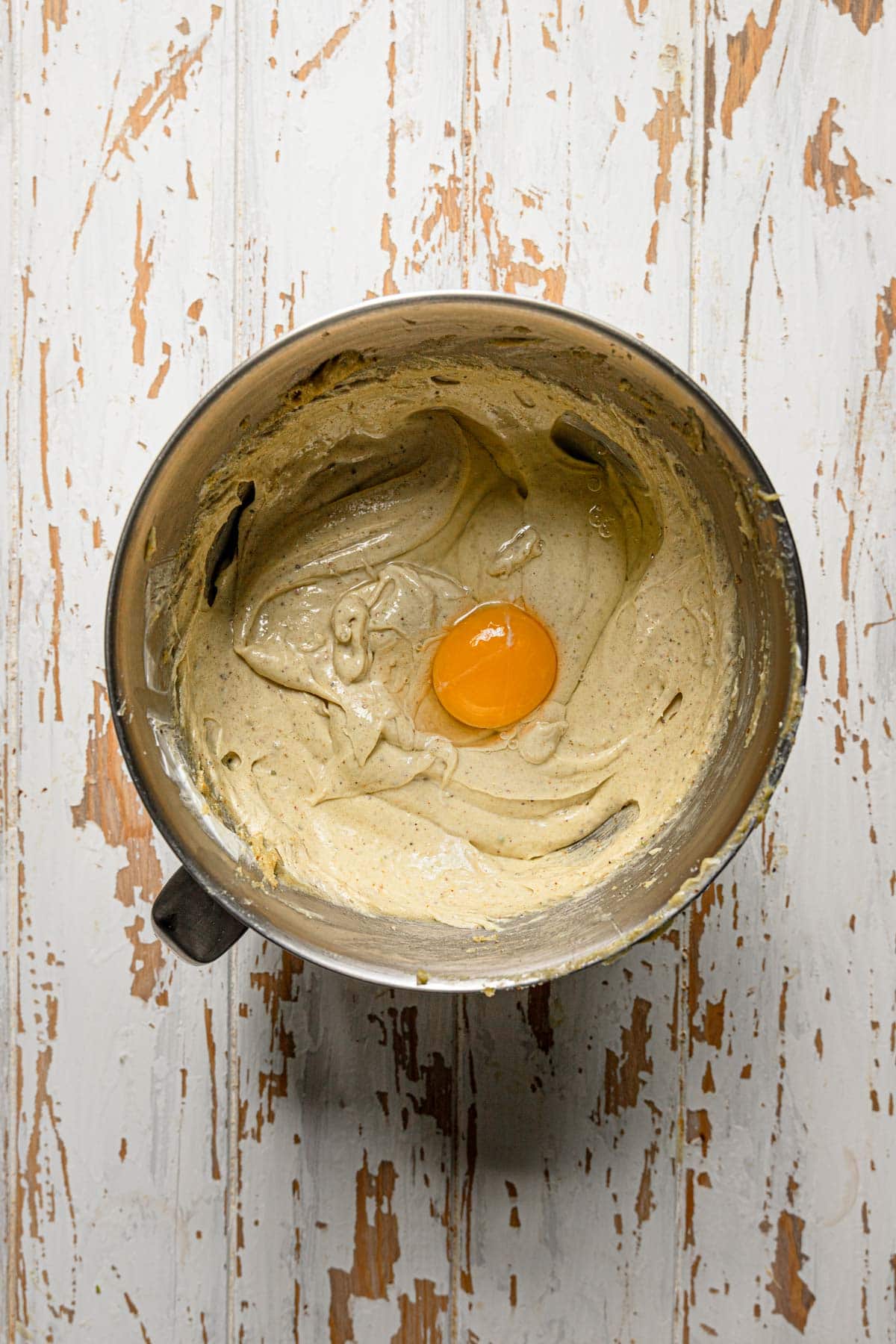 A stand mixer bowl with cake batter and an egg.