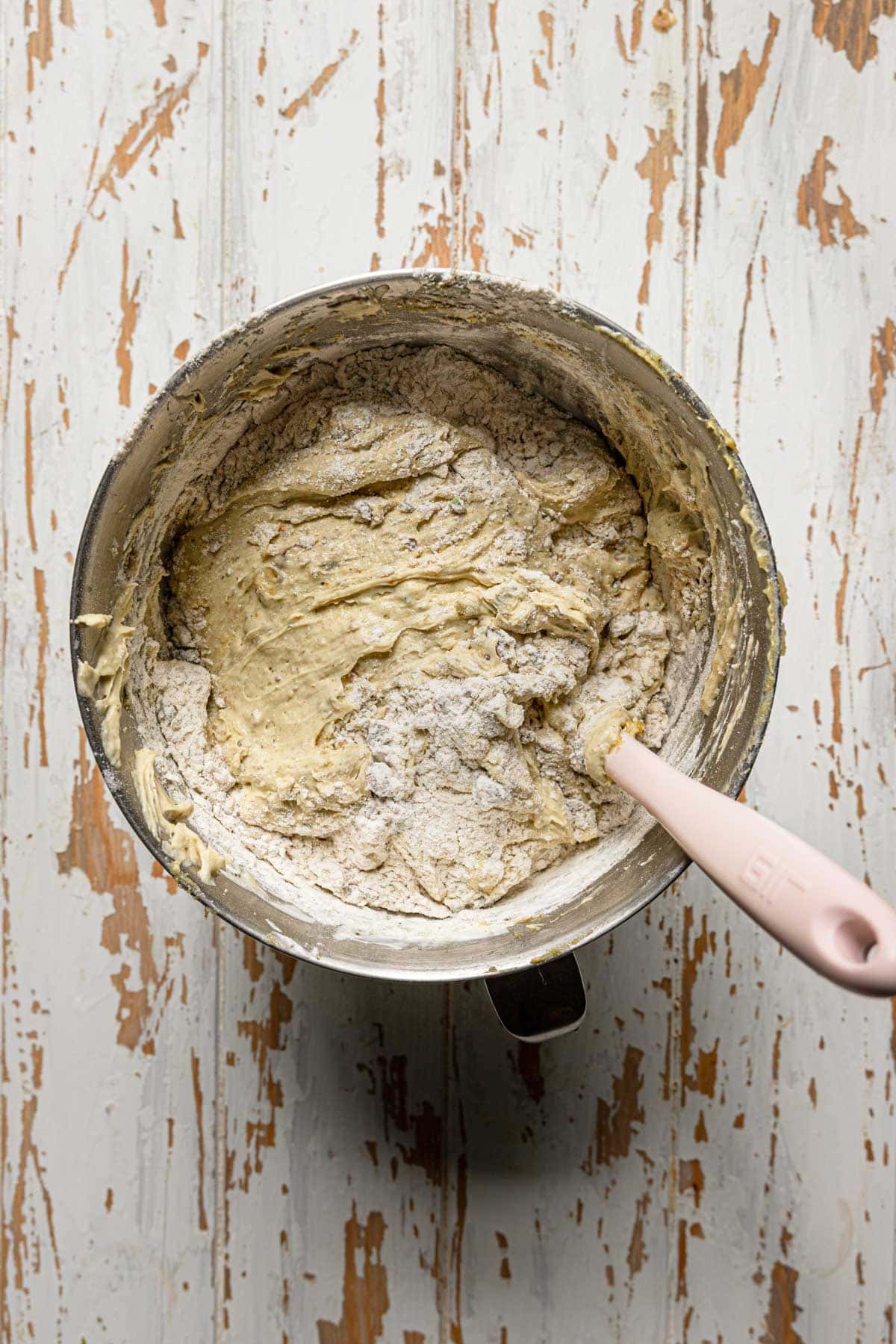 A stand mixer bowl with cake batter and a spatula mixing in the flour.