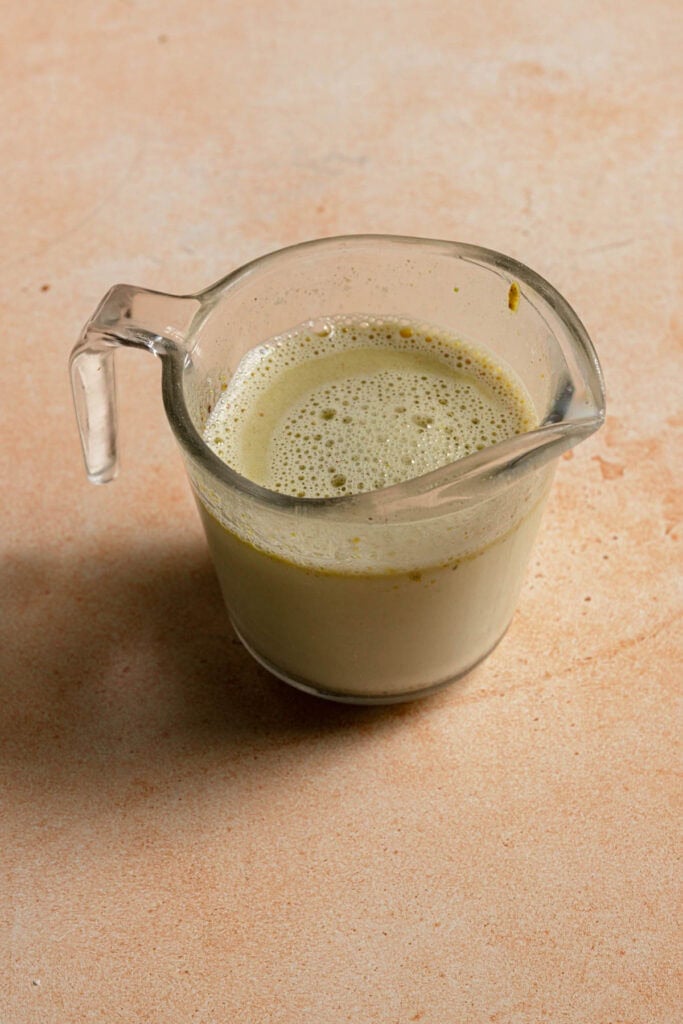 A measuring cup with milk, pistachio paste and a spoon.