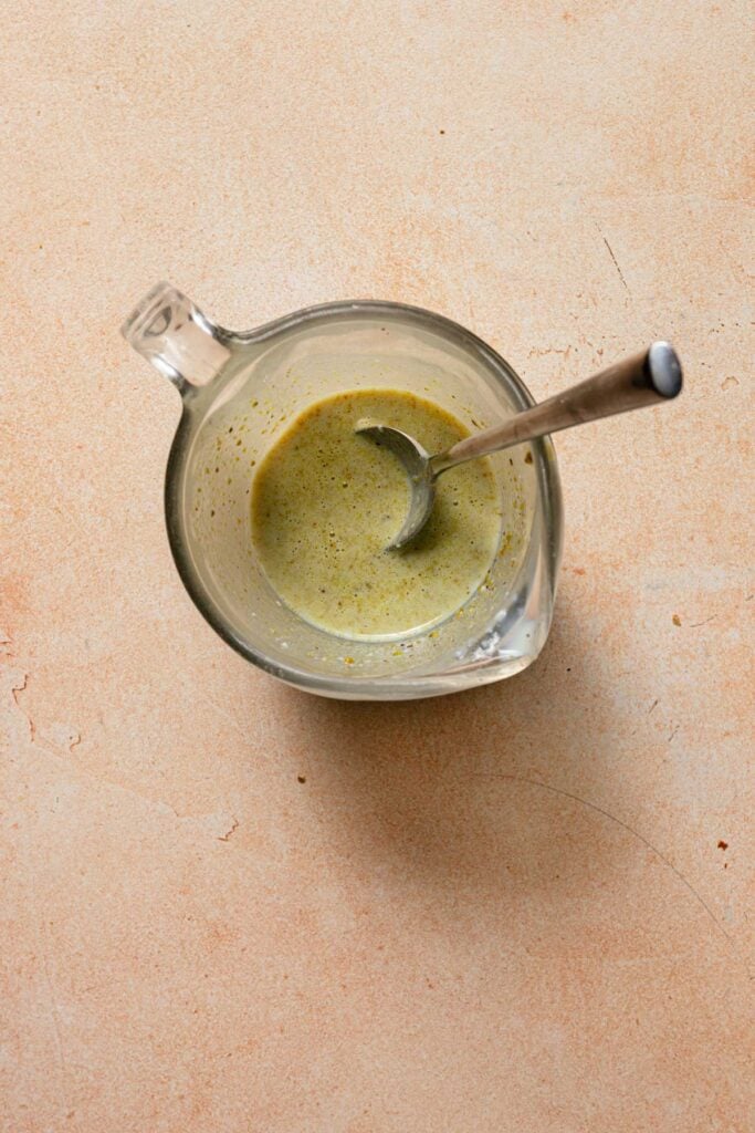 A measuring cup with milk, pistachio paste and a spoon.