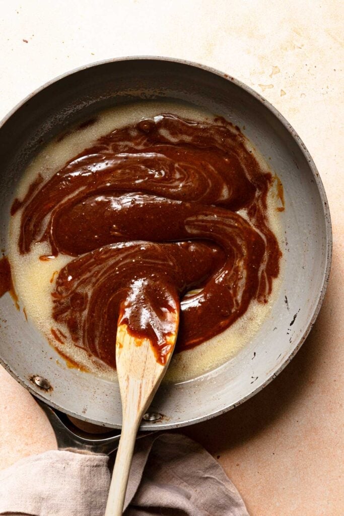 A wide skillet with pistachio caramel, melted butter and a wooden spoon.