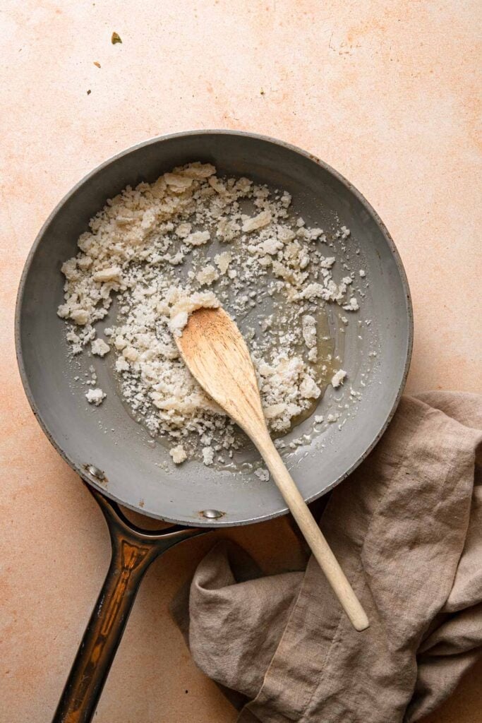 A wide skillet with clumped sugar ad a wooden spoon.