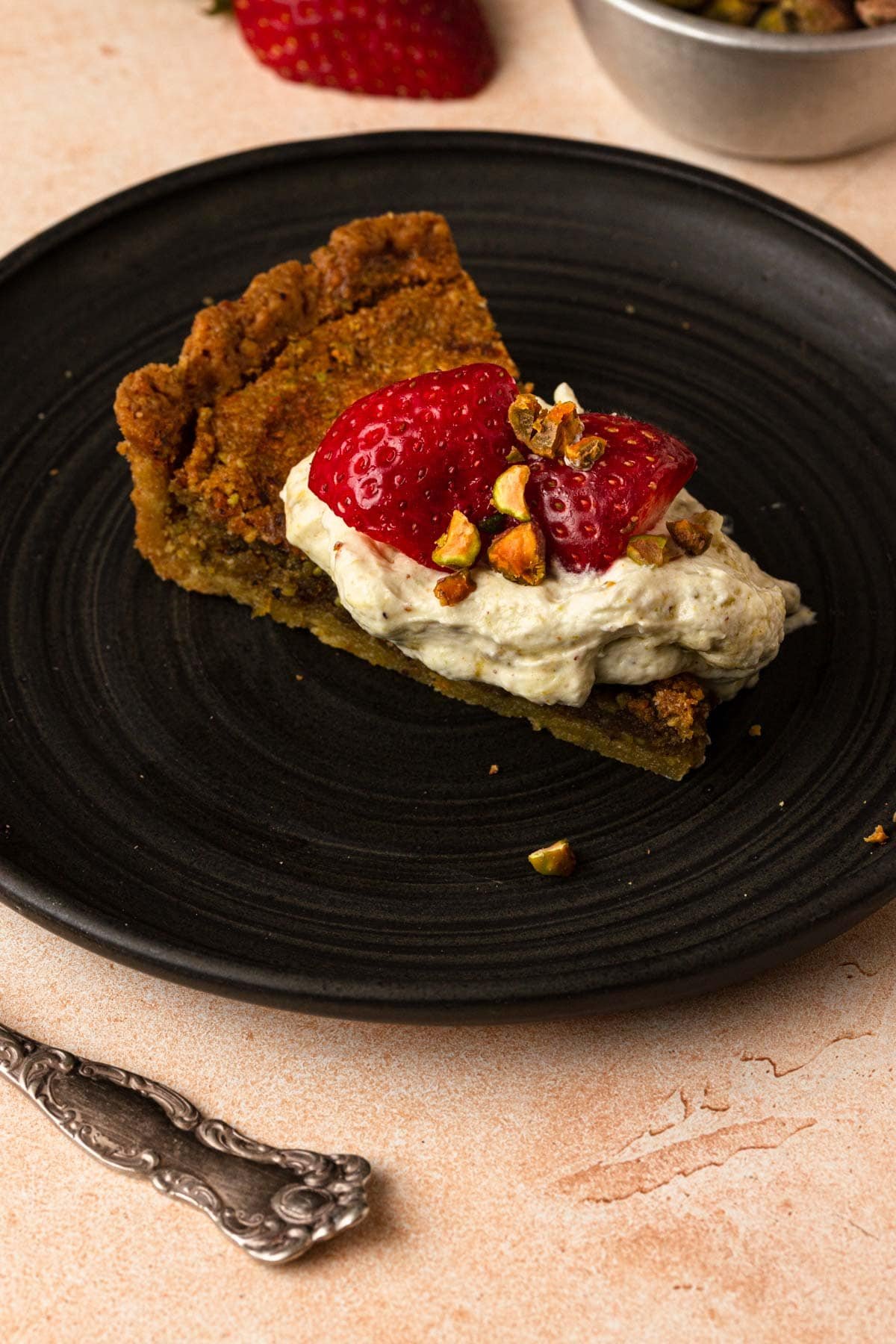 A piece of pistachio tart topped with whipped cream and fresh starwberries.