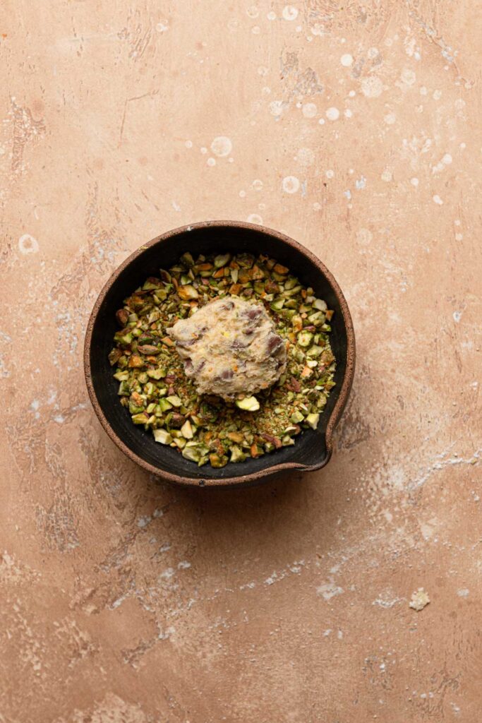 A bowl with chopped pistachio and a cookie dough ball.