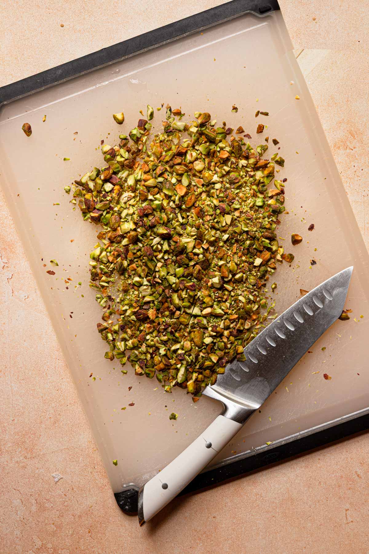 Chopped pistachios on a cutting board next to a large knife.