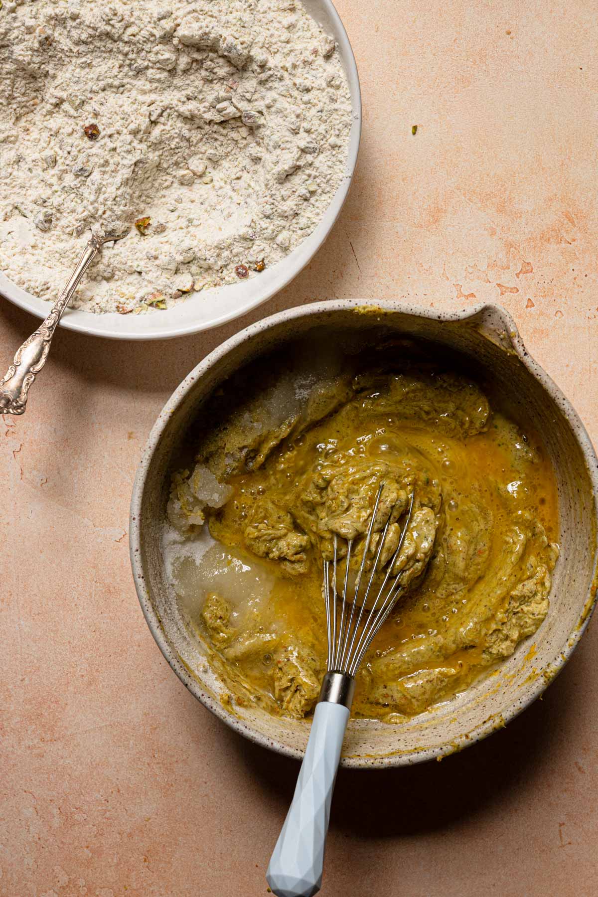 Two bowls, one with flour and another one with pistachio mixture and a whisk.