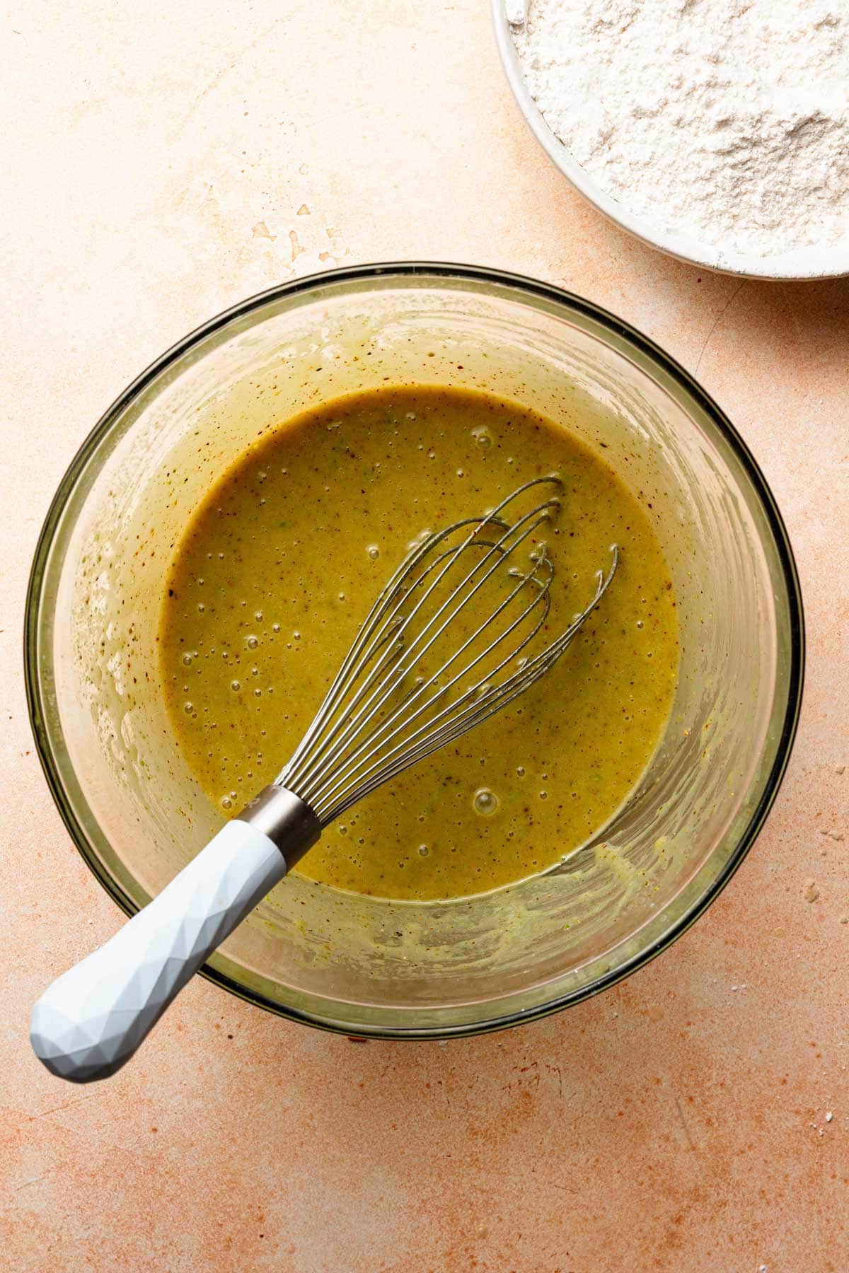 A bowl with pistachio yolk mixture for cake with a whisk.